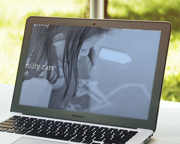 A cropped, blue-toned image of a young girl drawing on the ground with chalk, shown on the screen of a MacBook